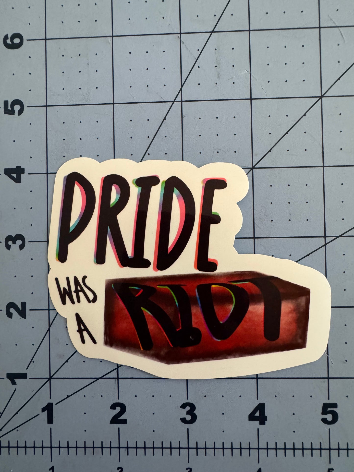 Sticker reading “Pride Was a Riot” with the word “Riot” stylized as a red brick. Available in holographic and classic white finish.
