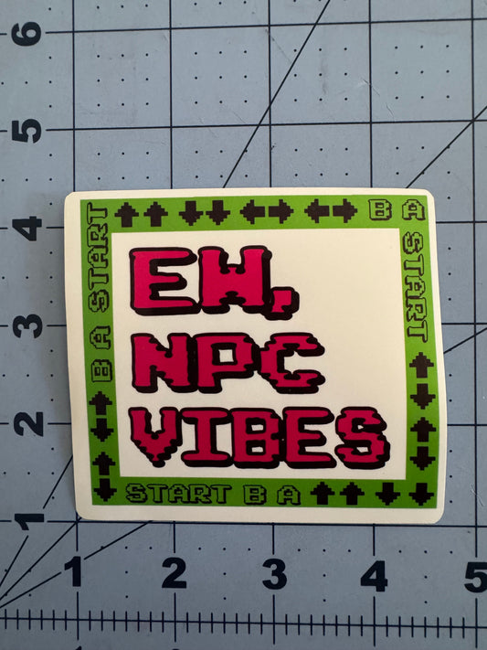 Two versions of a square sticker featuring pixelated text reading “Ew, NPC Vibes” in red on a white background. The border is bright green with black 8-bit arrow symbols and the words “START B A” repeated, referencing a classic video game controller pattern. One version has a standard white finish, the other has a holographic sheen. Stickers are shown on a blue grid cutting mat with inch measurements for scale.